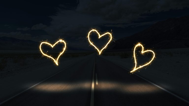 Three illuminated heart shapes created with sparklers over a dark road at night.