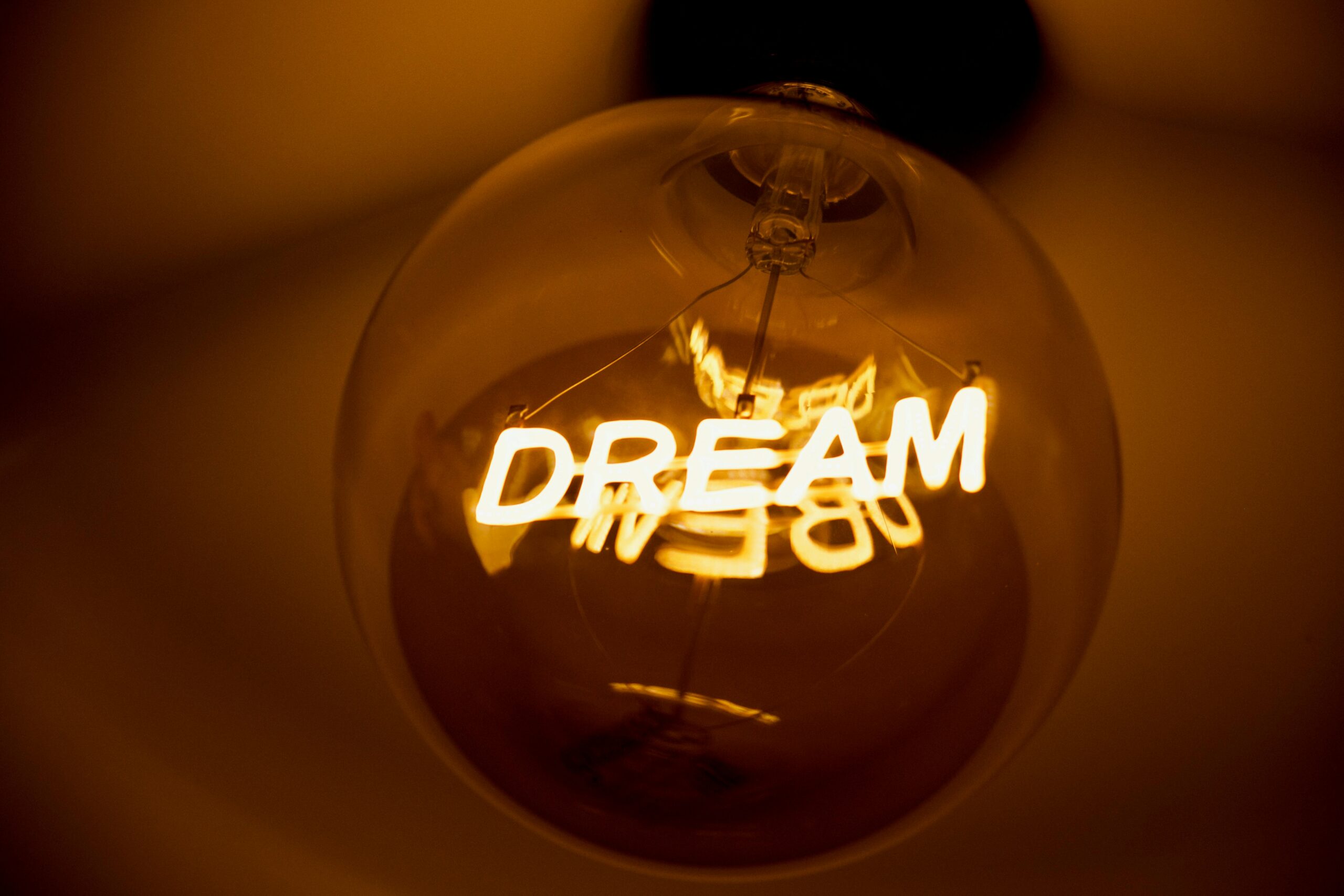 Close-up of an incandescent light bulb with 'Dream' glowing in warm light.