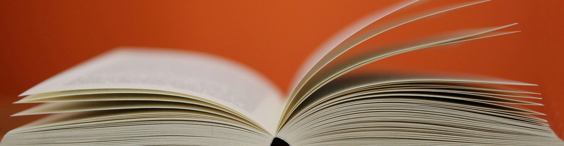 An open book with pages turning against a vibrant orange background, symbolizing knowledge and education.